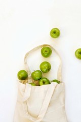 Reusable cotton textile bag with green apples on a white background. The concept of zero waste, green shopping. Top view with copy space for text.