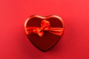 Red heart-shaped box with ribbon on red background