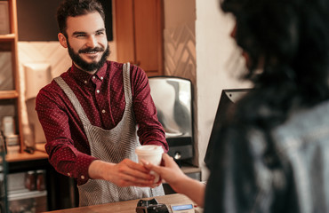 Friendly barista giving takeaway beverage to customer