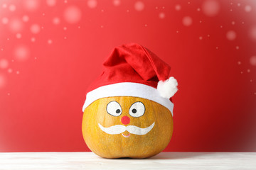 Pumpkin with mustache and red Santa hat against red background, copy space