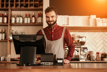 Cheerful bearded bartender near cash register - obrazy, fototapety, plakaty