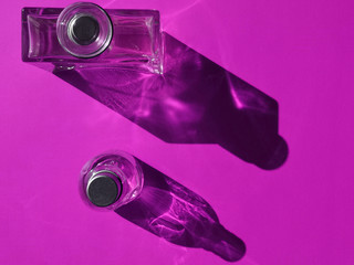 Composition of rectangular and round bottles. Abstract close-up photo of alcohol, perfume or pharmacy packaging design. Flat lay photo of glass objects on purple background with contrast shadows. 