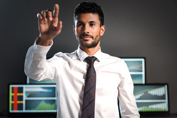 selective focus of bi-racial trader pointing with finger and computers on background
