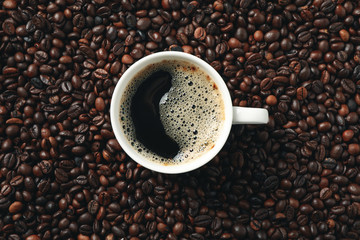 Cup of coffee on coffee beans background, top view