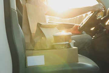 Blank box, coffee cups, paper packages and courier in car. Delivery