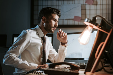 side view of handsome bi-racial trader using computer and sitting at table