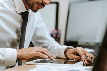 cropped view of bi-racial trader sitting at table and using digital tablet