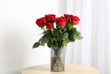 Vase with bouquet of red roses on wooden table, space for text
