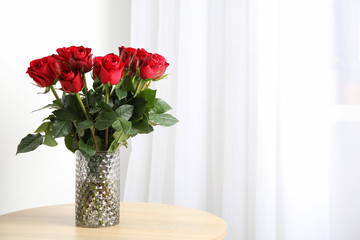 Vase with bouquet of red roses on wooden table, space for text