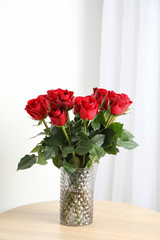 Vase with bouquet of red roses on wooden table, space for text