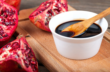 Homemade pomegranate sauce in a bowl with a spoon, fresh open pomegranate on a wooden background