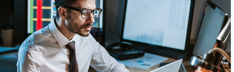 panoramic shot of bi-racial trader in glasses looking at computer