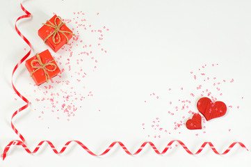 two red gift boxes in the upper left corner of the imag and two red wooden hearts in the lower right corner of the image are sprinkled with small shiny red hearts and two red shiny ribbons