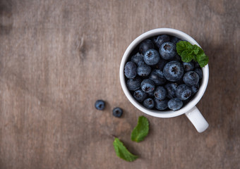 Fresh and sweet blueberry in cup with mint on brown wood background