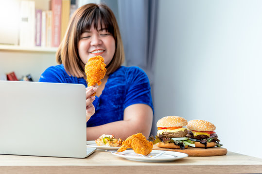 Asian fat women Happy to eating with the food she prepared Which has fried chicken, hamburger, while working using a note book, This picture focuses on fried chicken, to Cholesterol concept.