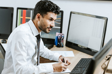 bi-racial trader looking at computer and holding pen in office