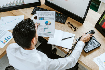 overhead view of bi-racial trader looking at paper and holding handset