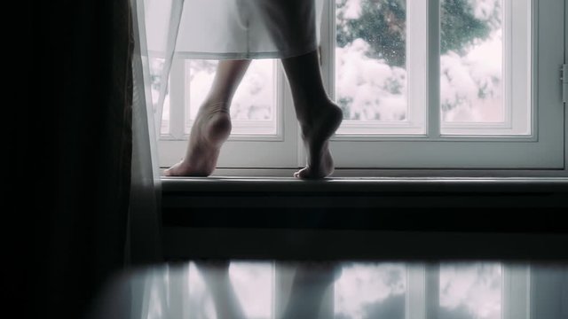 Girl walks barefoot on a windowsill in a winter day
