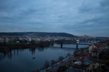 Fototapeta premium Winter panorama from Vysehrad Castle to the evening city of Prague, residential areas, the Vltava River, moorings with boats and boats and city transport.