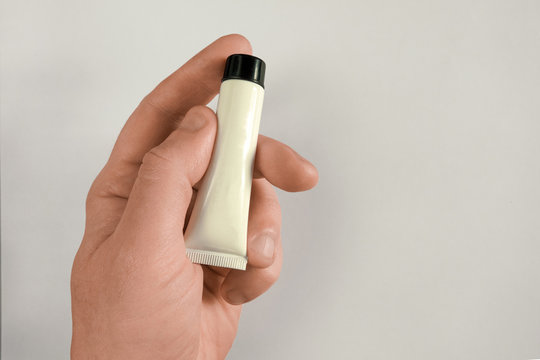 Man hand holds tube with cream, gel or paste. Mock-up on light background with shadow and copy space. Middle aged man body care concept closeup image