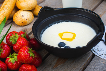 Traditional breakfast milk porridge with butter and berries on a wooden table.