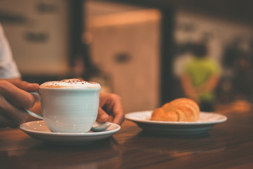 hands hold cup of coffee and spoon in the dish.