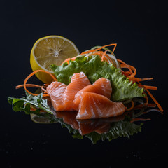 salmon's sashimi with salad and lemon on black background