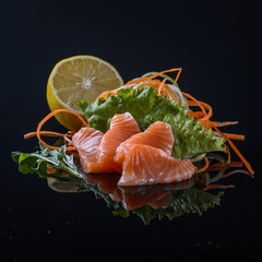 salmon's sashimi with salad and lemon on black background