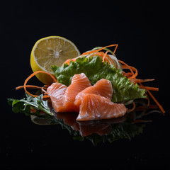 salmon's sashimi with salad and lemon on black background