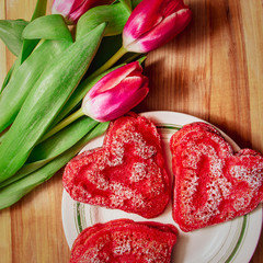 Obraz na płótnie Canvas Red heart shaped pancakes made with love for valentines day and tulips on wooden background