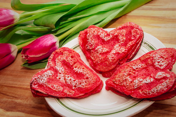 Red heart shaped pancakes made with love for valentines day and tulips on wooden background
