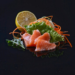 salmon's sashimi with salad and lemon on black background