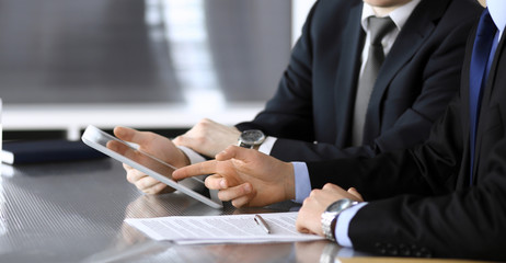 Businessman using tablet computer and work together with his colleague or partner at the glass desk in modern office, close-up. Unknown business people at meeting