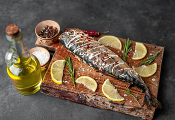 baked mackerel on a cutting board with lemon and spices on a stone background, ready to eat