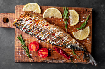 baked mackerel on a cutting board with lemon and spices on a stone background, ready to eat