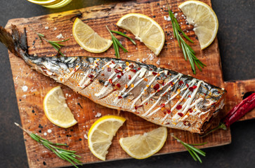 baked mackerel on a cutting board with lemon and spices on a stone background, ready to eat