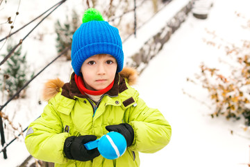 Playful little boy making snowballs in back yard. Child plays with snow outdoors. Winter holidays