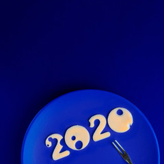 Figures 2020 made of cheese with holes on blue plate with small fork on empty background, top view, Square, copy space. Christmas and New year concept for restaurant, Classic, monochrome, trend 2020