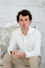 Portrait of a young man. He sits in a chair. Black curly hair.