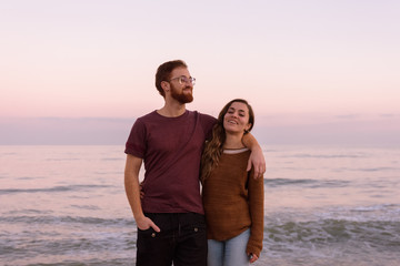 Young caucasian couple hugging and laughing together at a sunrise on the beach, redhead boy and blonde girl