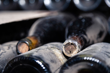 Closeup dark dusty wine bottles with old crumbly cork. Long aging, musty winery vault, rare ancient...