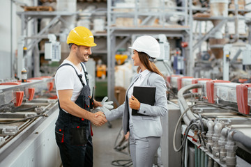 Architect and worker working on project. Colleagues handshaking in factory.	