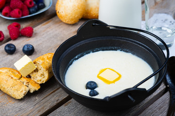 Traditional breakfast milk porridge with butter and berries on a wooden table.
