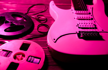 White electric guitar on wooden background. Old reel-to-reel tape recorder cassettes. Retro music concept. Red shadows.