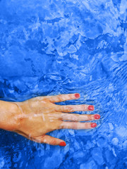 Obraz na płótnie Canvas Classic blue color of 2020. Water surface with ripples and female hand with red manicure.