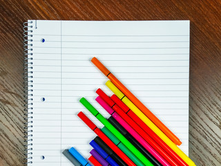 Empty white notebook with lines and colorful pens on top for taking notes on the lectures and better organization while studying and writing