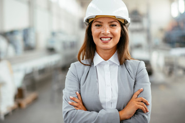 Portrait of businesswoman in factory. Young female architect with helmet in suit.	