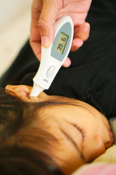 Mother measuring temperature of her ill kid girl.Sick child with high fever laying in sofa and mother holding thermometer.Clinical digital ear thermometer scan in hand of a physician