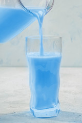 Closeup beverage toned in Trendy 2020 Classic Blue color, is pouring from clear glass decanter into wavy figured glass. 