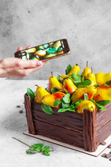 girl photographs a pear cake with a smartphone. Birthday cake in the form of a chocolate box filled with pears made from mousse